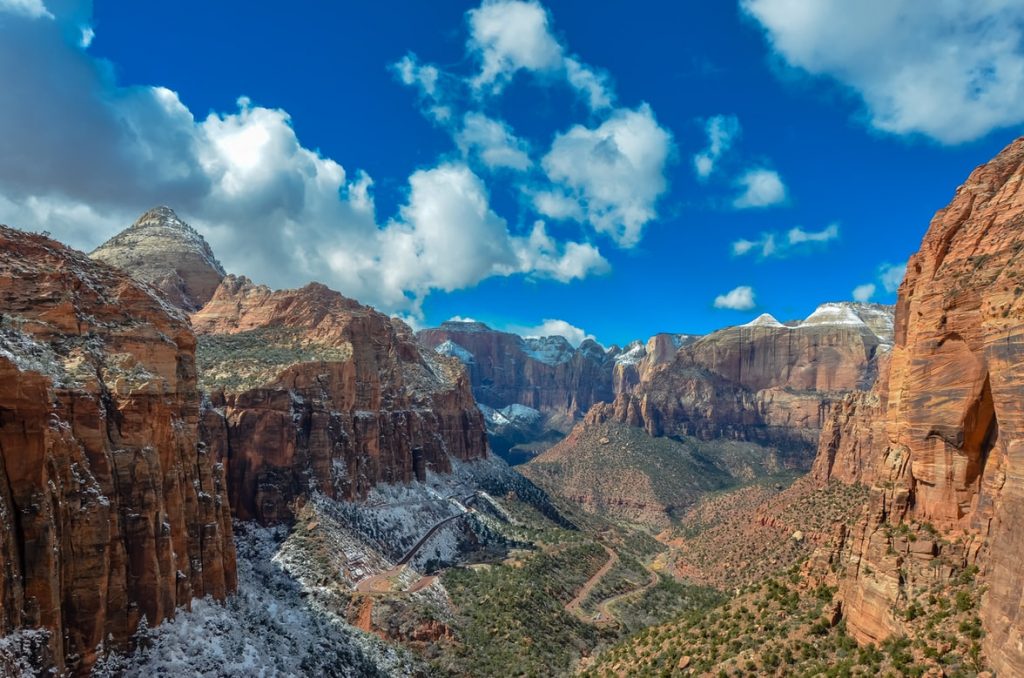 View of the vast canyon and valley of Zion National Park with snow dusted cliff faces and a bright blue sky.