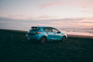A Blue Mazda on the sandy beach during the sunset